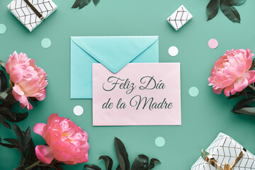 Feliz Dia de la Madre means Happy Mother's Day in Spanish. Pink peony flowers, wrapped gifts tied with gold ribbon, confetti. Mint green, pink floral decor. Pastel colors, lat lay, top view on paper.