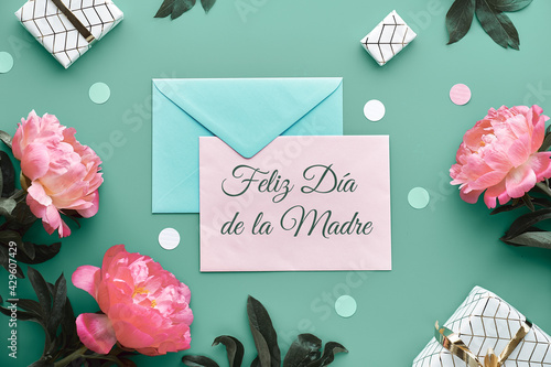 Feliz Dia de la Madre means Happy Mother's Day in Spanish. Pink peony flowers, wrapped gifts tied with gold ribbon, confetti. Mint green, pink floral decor. Pastel colors, lat lay, top view on paper. photo