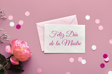 Feliz Dia de la Madre means Happy Mother's Day in Spanish. Pink peony flower, greeting card, envelope and paper confetti, circles. Monochrome minimal pink floral arrangement, top view, flat lay.