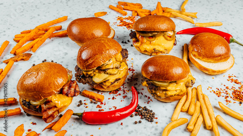 Tableau sur toile A closeup shot of tasty smash burgers, French fries, and red spicy peppers on th