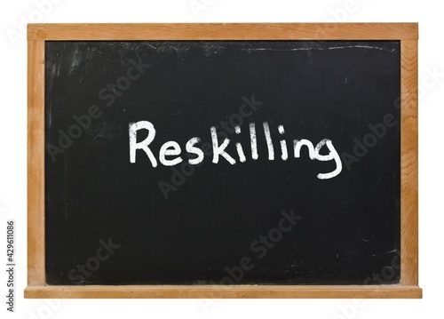 Reskilling written in white chalk on a black chalkboard isolated on white