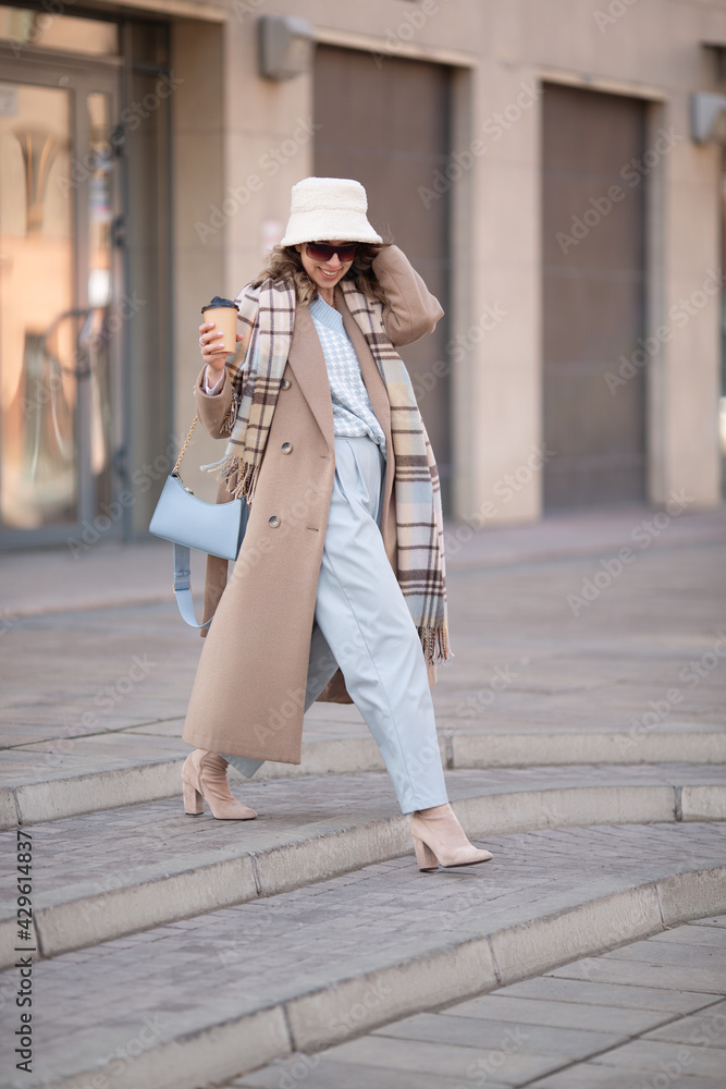woman in fashionable clothes walks through the city. Coat and headwear
