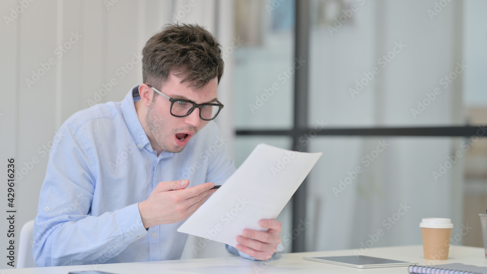 Young Man Reacting to Loss While Reading Documents Young Man Reacting to Loss While Reading Documents
