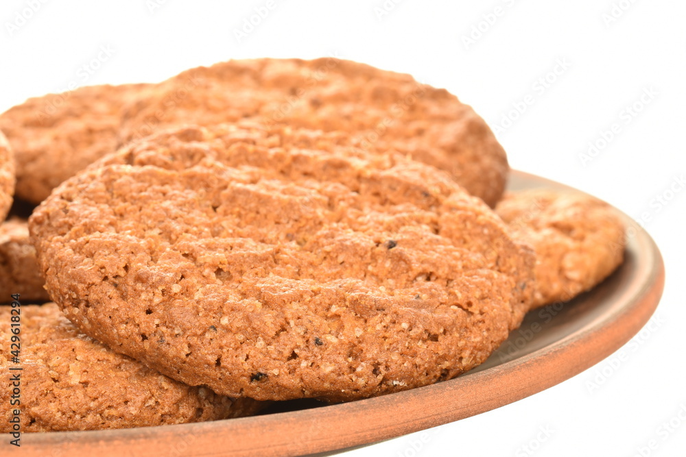 Three fragrant dark brown, oatmeal cookies on earthenware, close-up, isolated on white. Three fragrant dark brown, oatmeal cookies on earthenware, close-up, isolated on white.