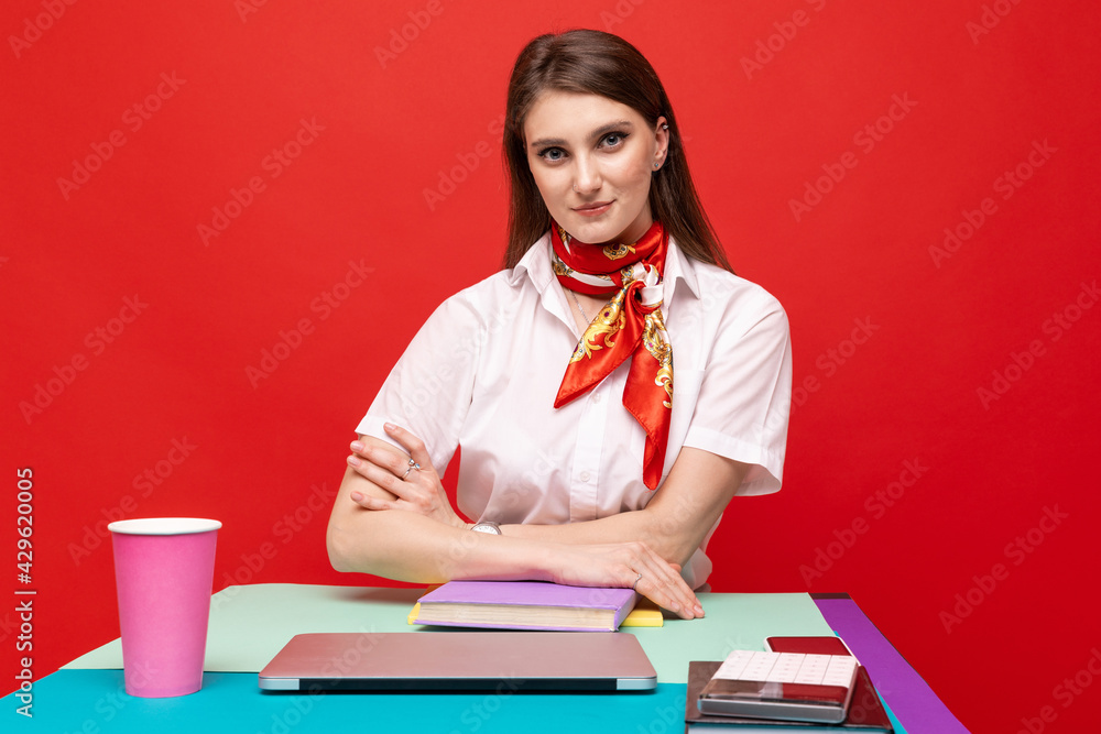 Portrait of a young woman in a white shirt working at a desk on a red background