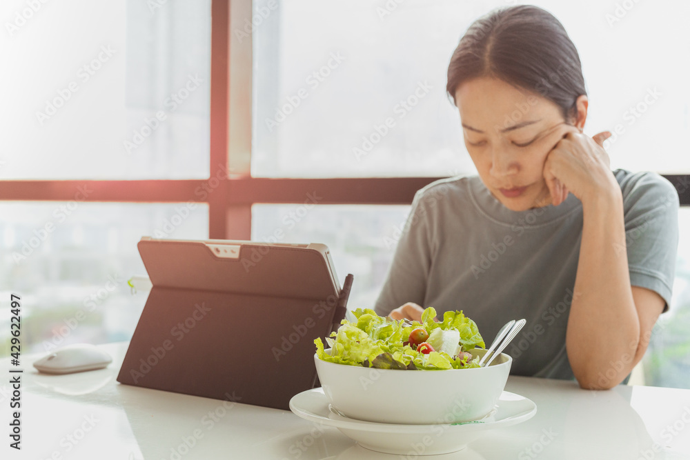 Selected focus on bowl of vegetable salad with woman working on laptop.