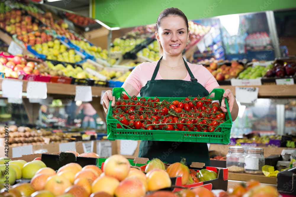 Portrait of smiling female in store with crate filled with fresh tomatoes