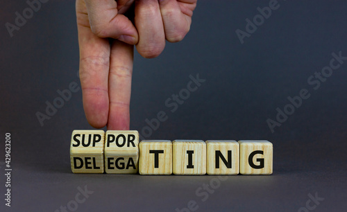 Delegating or supporting leadership style symbol. Businessman turns cubes, changes words supporting to delegating. Beautiful grey background, copy space. Business, delegating or supporting concept.