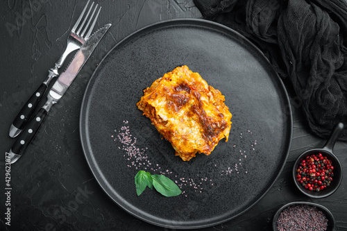 Baked meat lasagna, on plate, on black stone background, top view, flat lay