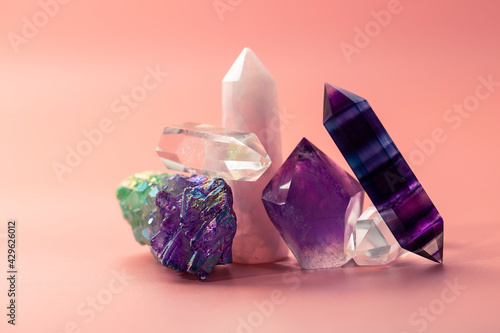 Various faceted crystals for healing and magical practices. A bunch of beautiful semi-precious stones. Amethyst, rose quartz, fluorite, rock crystal on a pastel pink background