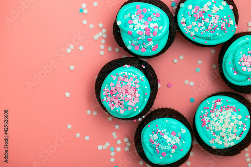 Chocolate cupcakes decorated with turquoise and pink icing sugar and sprinkles at home. Festive sweet food close-up on a pink background. Top view