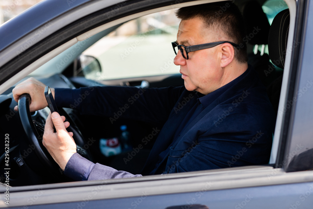 Middle-aged businessman sitting in his parked car and uses a mobile phone in a car.