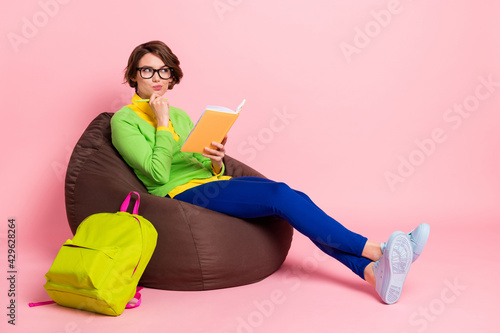 Full body photo of brunette bob haired schoolgirl wear green shirt hold notebook think sit write homework isolated on pink color background
