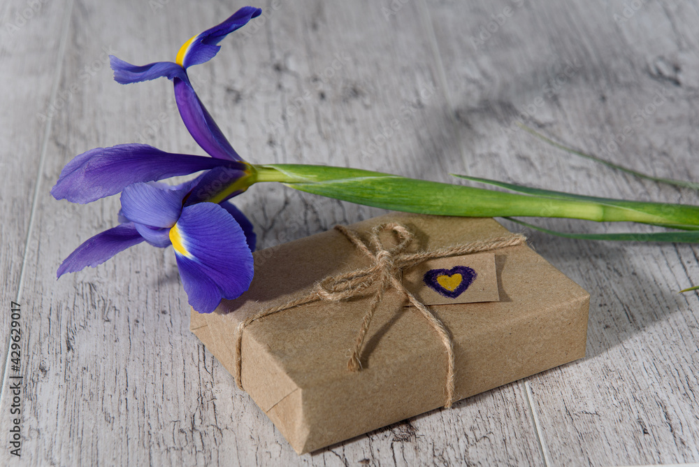 Gift box wrapped with kraft paper, hand drawn small heart and iris flower. Happy Mother's Day, Valentine's Day or birthday background. Greeting card.