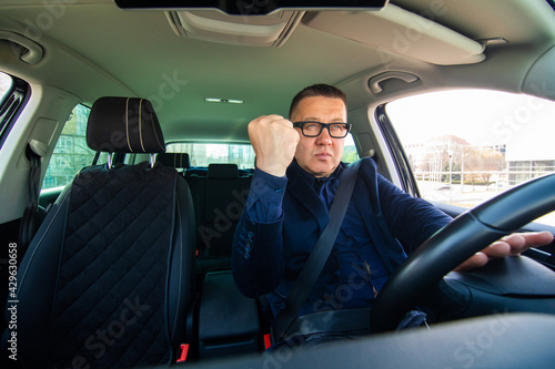 Angry man looking outside from car window with fist up