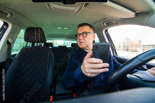 Middle aged man with eyeglasses sitting in his car and reading message on smart phone while witting in traffic. © F8  \ Suport Ukraine