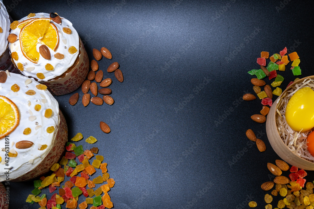 Traditional Easter cakes on dark blue background. Migdal, candied fruits, colorful eggs and raisins, decor. Orthodox treat. Top down view. Copy space for text Traditional Easter cakes on dark blue background. Migdal, candied fruits, colorful eggs and raisins, decor. Orthodox treat. Top down view. Copy space for text