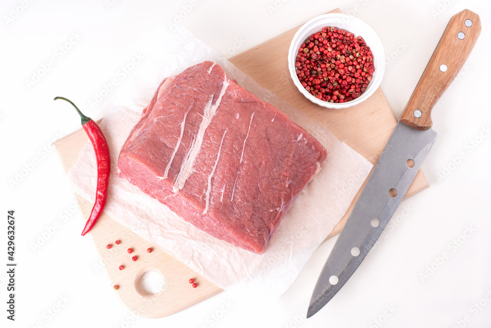 Raw veal meat on a cutting board with spices and a knife on a white plate.
