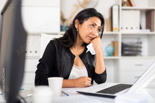 Portrait of disappointed crying latin american female office employee during work with laptop and documents