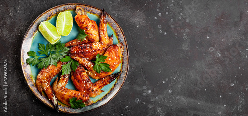 Web banner. Baked chicken wings with sesame seeds, parsley and lime on a plate top view, free space for text