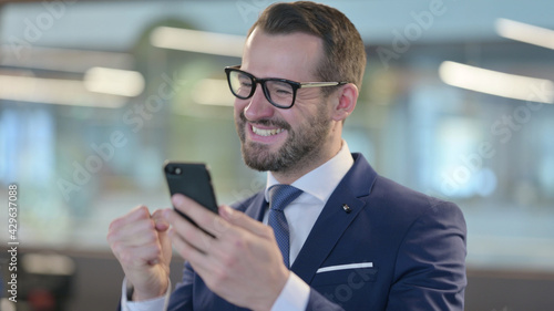 Portrait of Middle Aged Businessman Celebrating on Smartphone