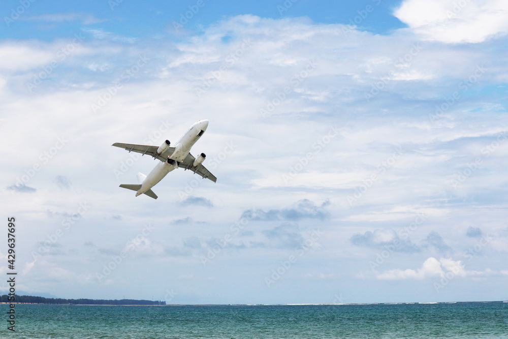 Airplane flies over the sea and coast on white clouds background. Commercial plane taking off and gaining altitude, vacation and travel concept