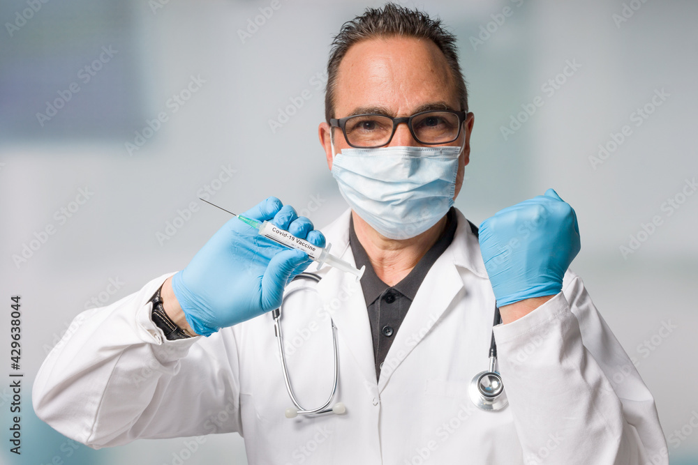 happy doctor with medical face mask and medical gloves presenting a syringe pulled up with a coronavirus vaccine and makes a powerful gesture happy doctor with medical face mask and medical gloves presenting a syringe pulled up with a coronavirus vaccine and makes a powerful gesture