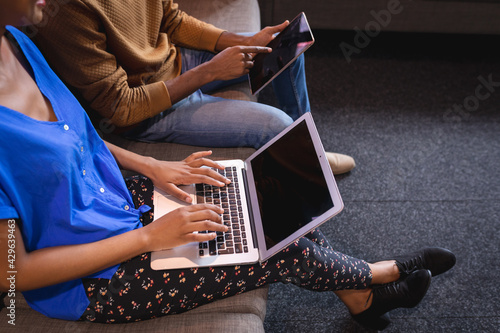 Diverse male and female colleagues working sititng on sofa in office using computer and tablet photo