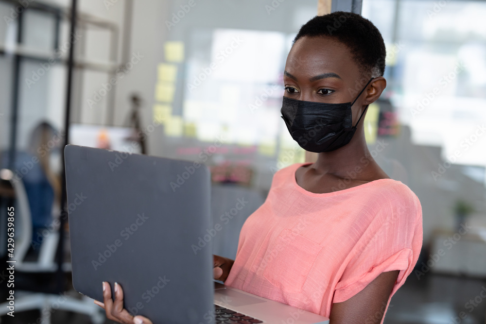 Obraz premium African american businesswoman wearing mask using laptop computer