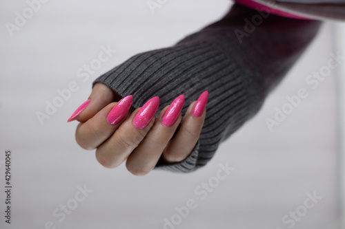 Photo Female hand with long nails and a bottle bright neon pink red color nail polish