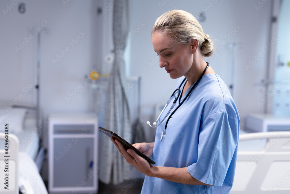 Serious caucasian female doctor in hospital wearing scrubs and stethoscope using tablet Serious caucasian female doctor in hospital wearing scrubs and stethoscope using tablet