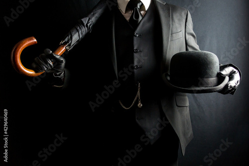 Portrait of Businessman in Dark Suit Holding Umbrella and Bowler Hat. Concept of Classic British Gentleman. Retro Style and Vintage Fashion. photo