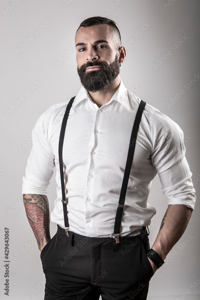 Uomo moro con la barba con camicia bianca e bretelle nere, guarda serio ,  isolato su sfondo Stock Photo | Adobe Stock