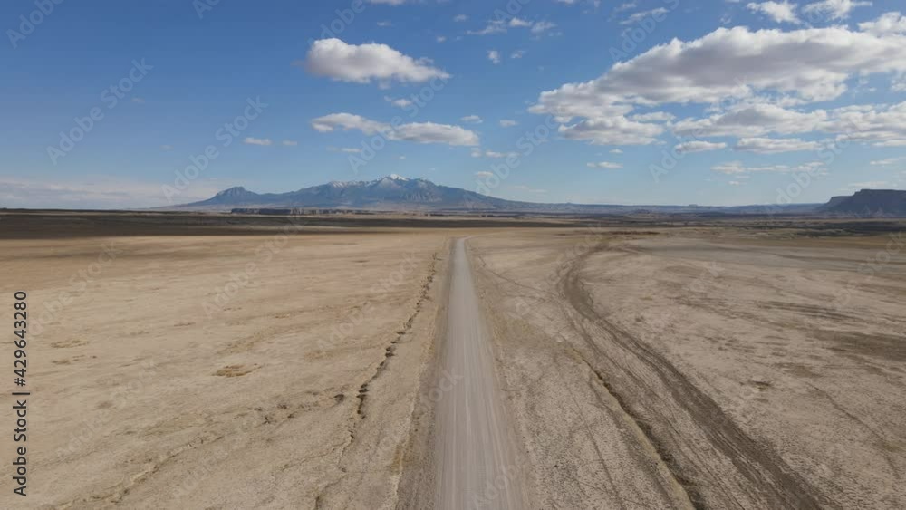 Flying drone over empty desert road with snow capped mountain in the distance Flying drone over empty desert road with snow capped mountain in the distance