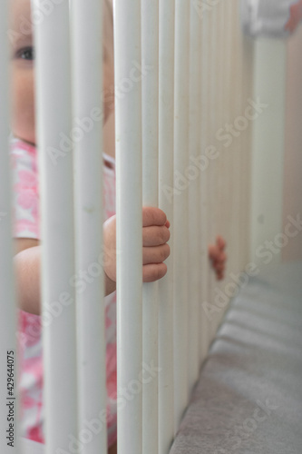 View from the inside of the crib; toddler pulling up to stand holding onto crib rails