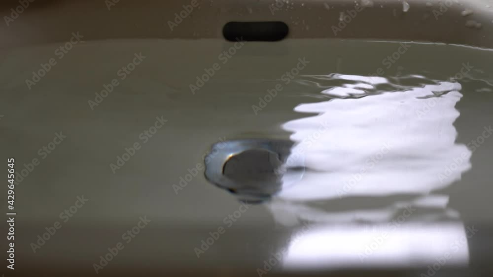 Close up on sink. The sink is full of water. Water drops slowly drip