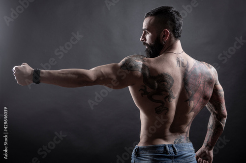 Uomo moro muscoloso e tatuato fa una posa mostrando il braccio e la schiena , isolato su sfondo nero 