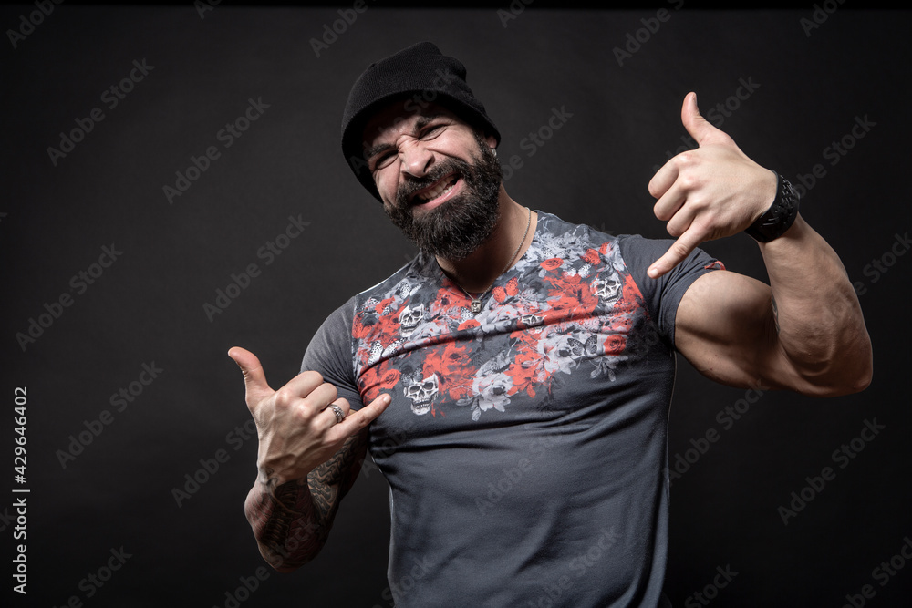 Φωτογραφία Uomo moro muscoloso con maglietta color fantasia e cappellino in lana, fa il ges