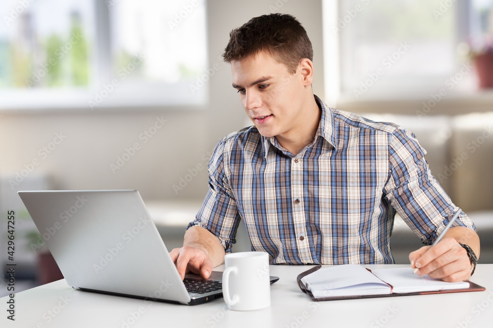 A happy young man works on his laptop with coffee at the table A happy young man works on his laptop with coffee at the table