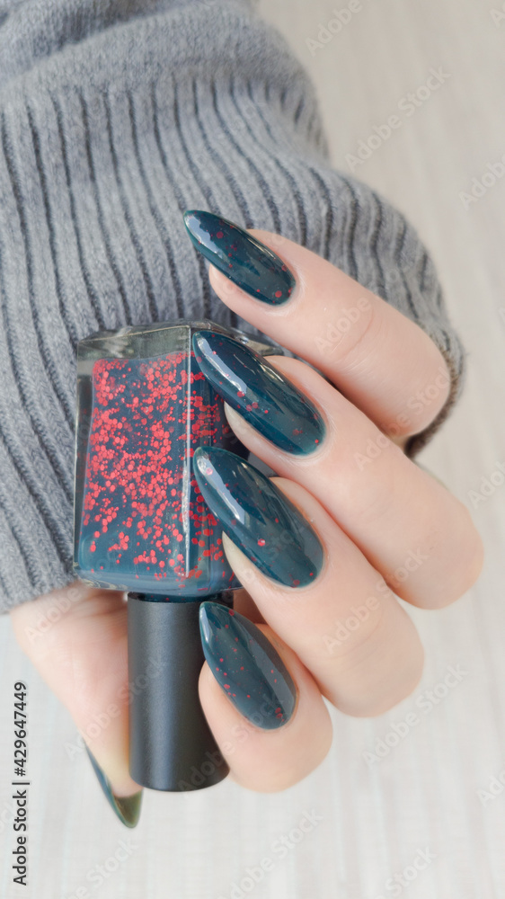 Female hand with long nails and dark blue green teal and red manicure holds  a bottle of nail polish Stock Photo | Adobe Stock