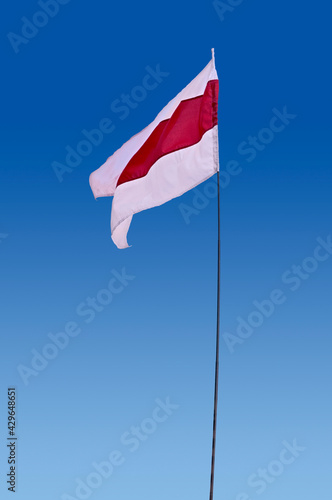 Isolated waving Belarusian national flag on blue sky background. White-red-white flag. A symbol of peaceful protests in Belarus against the dictatorship after presidential elections.