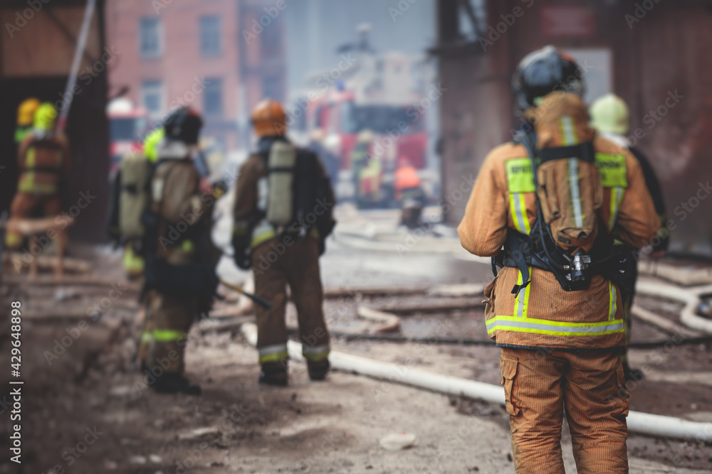 Firefighters put out large massive fire blaze, group of fire men in uniform during fire fighting operation in the city streets, firefighters with the fire engine truck fighting vehicle Firefighters put out large massive fire blaze, group of fire men in uniform during fire fighting operation in the city streets, firefighters with the fire engine truck fighting vehicle