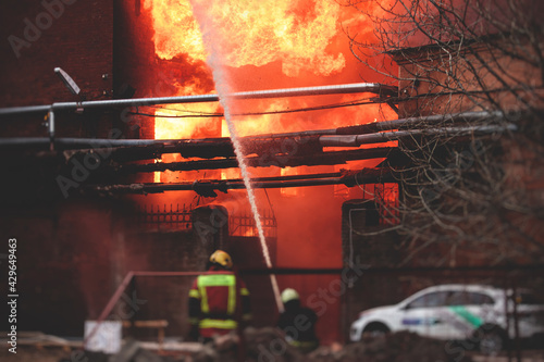 Фотография Firefighters put out large massive fire blaze, group of fire men in uniform duri