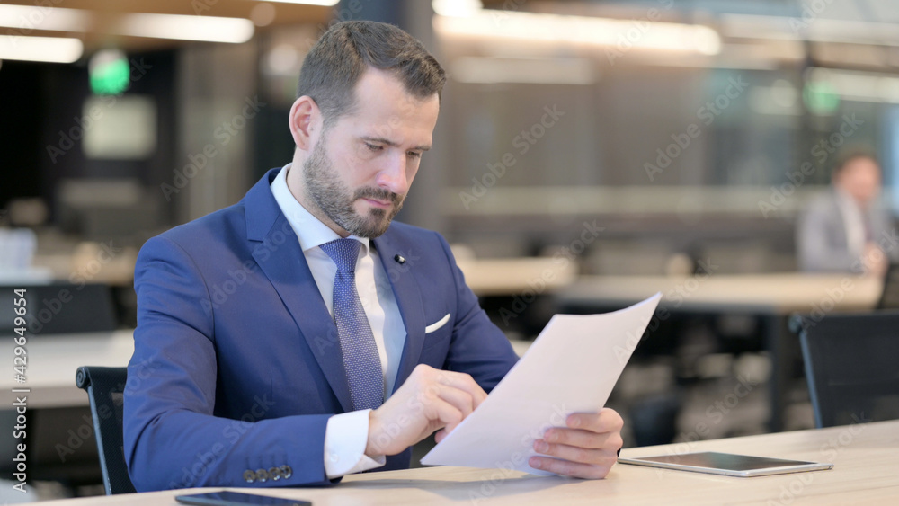 Middle Aged Businessman Reading Documents in Office Middle Aged Businessman Reading Documents in Office