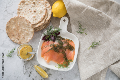 Gravlax Graved Lachs, ein roh gebeizter Fisch mit Dill auf Platte mit Hovmästarsås Senf Soße, Knäckebrot, Zitrone und Leinen Tuch auf hell Marmor Hintergrund photo