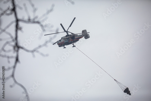 Fototapeta Naklejka Na Ścianę i Meble -  Fire fighting helicopter silhouette with bambi bucket for сarrying water to put out a massive building city fire, process of put out a large blaze bush fire wildifre, aerial firefighting with chopper