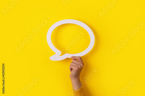 hand holding dialogue bubble over yellow background