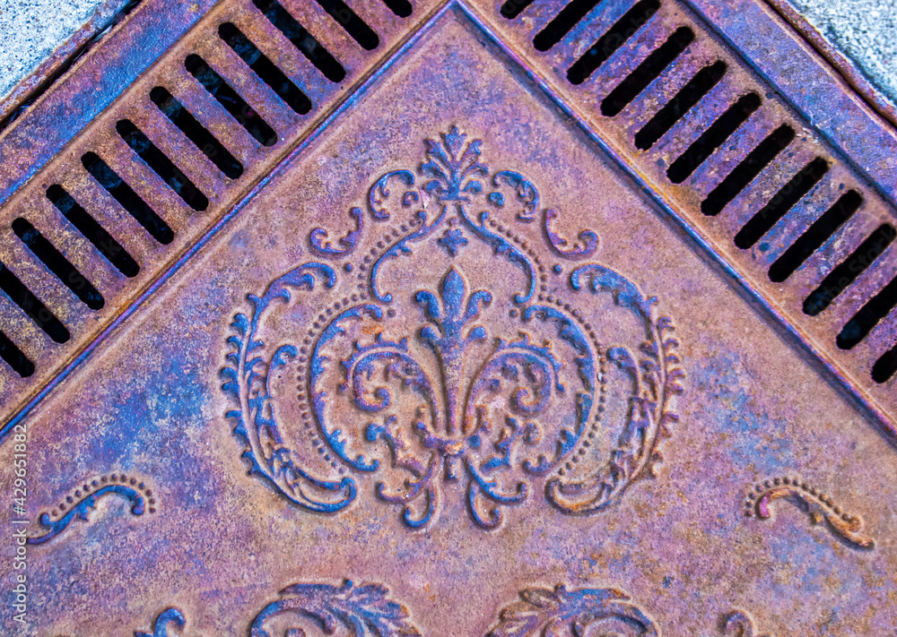 Vintage ornamental metal sidewalk grate - view from above on angle grainy rusted grungy and colorful.