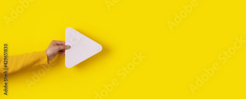 hand holding media player button icon over trendy yellow background, panoramic layout photo