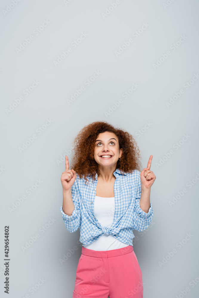 excited woman looking up and pointing with fingers on grey background excited woman looking up and pointing with fingers on grey background